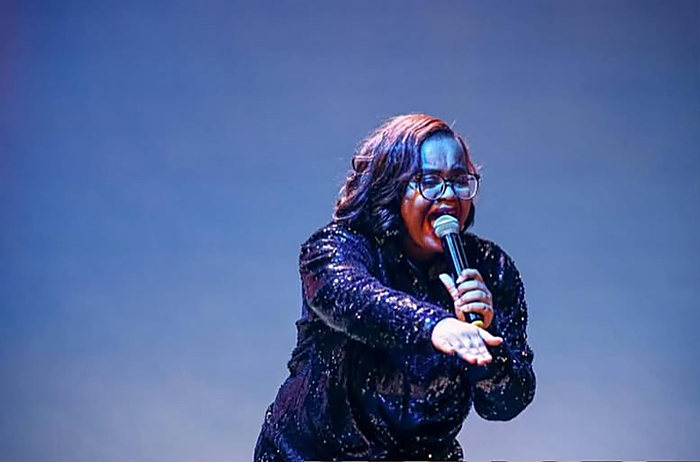 A singer on stage in a sequined jacket, singing into the microphone under blue light