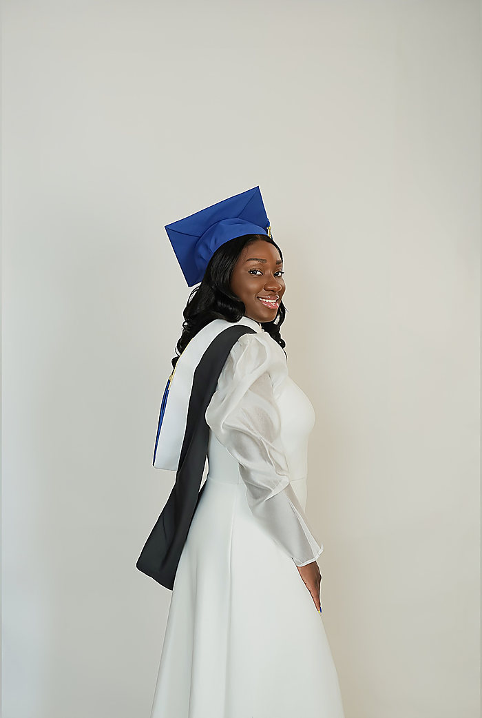 A graduate on gray: a blue cap, a white dress and a black and white stole