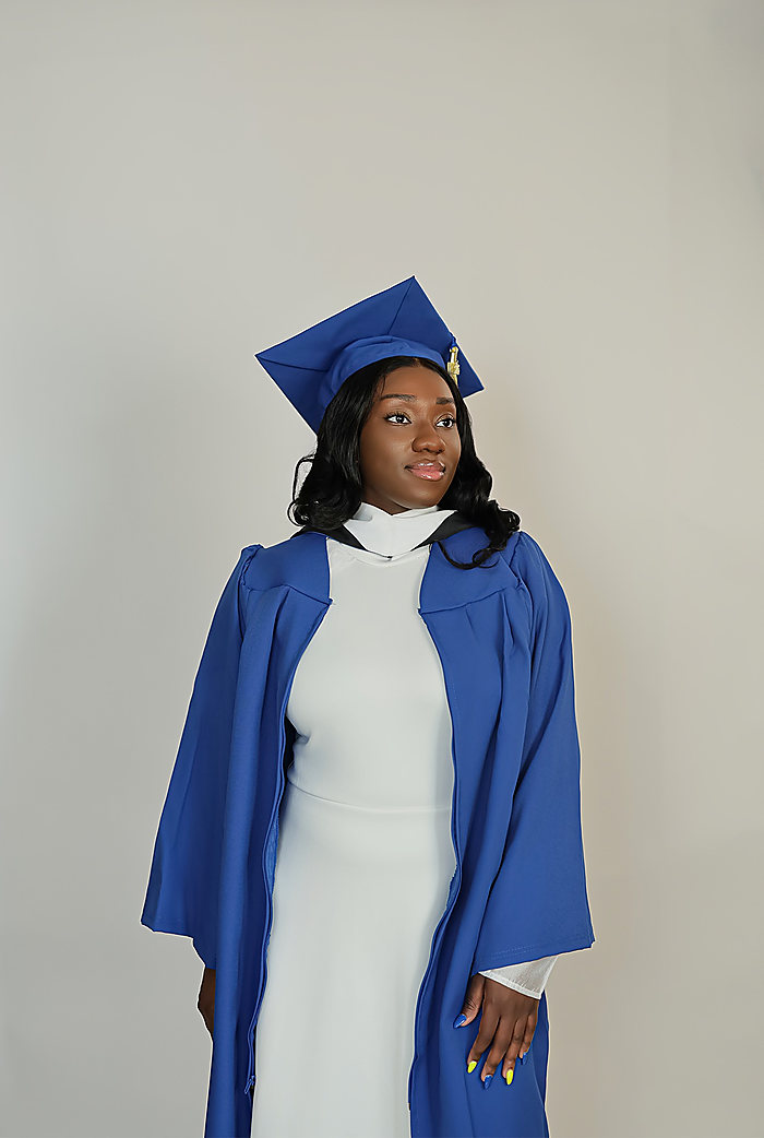 A graduate on gray in a royal blue gown and cap over a white dress