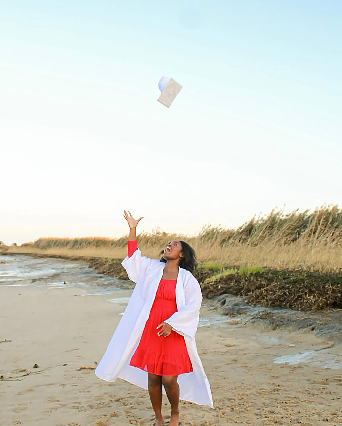 A graduate on the beach tossing her cap into the sky: a white gown over a red dress