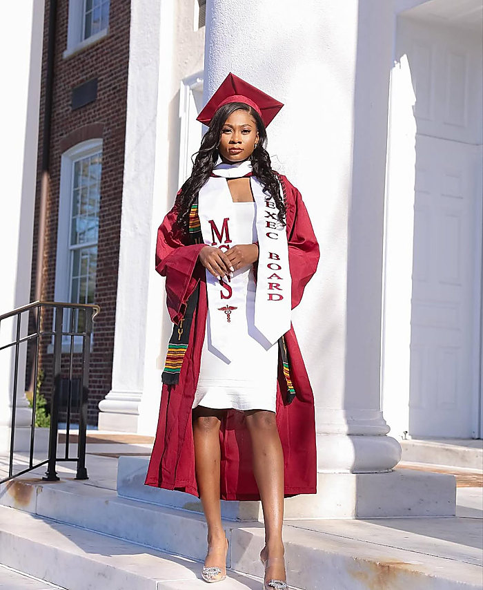A graduate on white steps between columns: a maroon gown over a white dress and two stoles