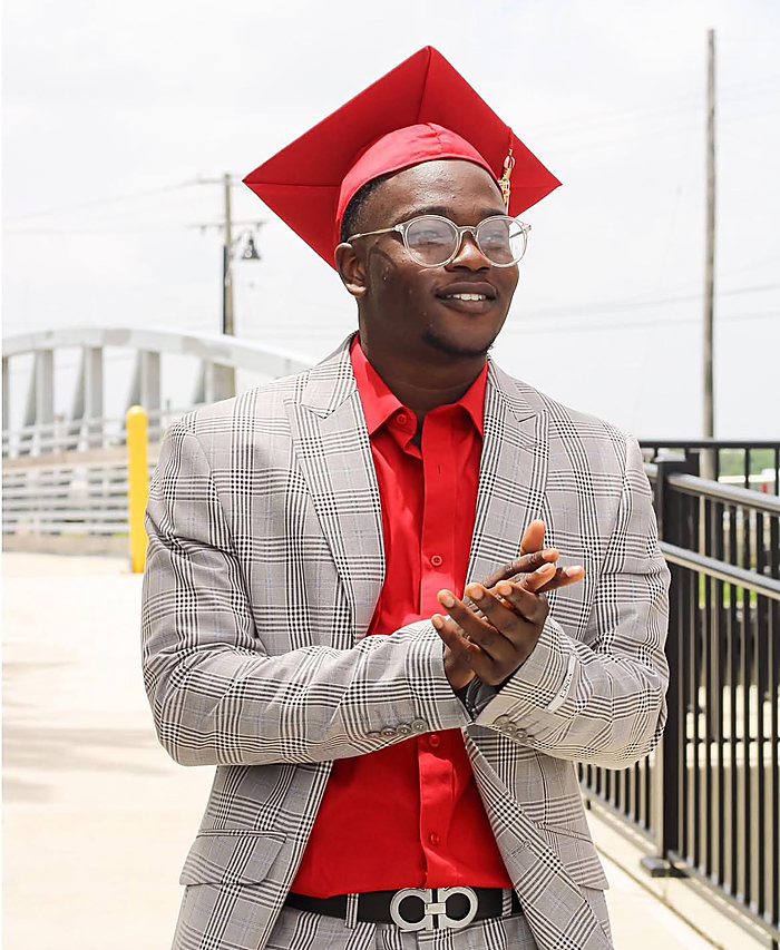 A graduate in a red cap, a gray plaid jacket and a red shirt, clapping on a bridge walkway