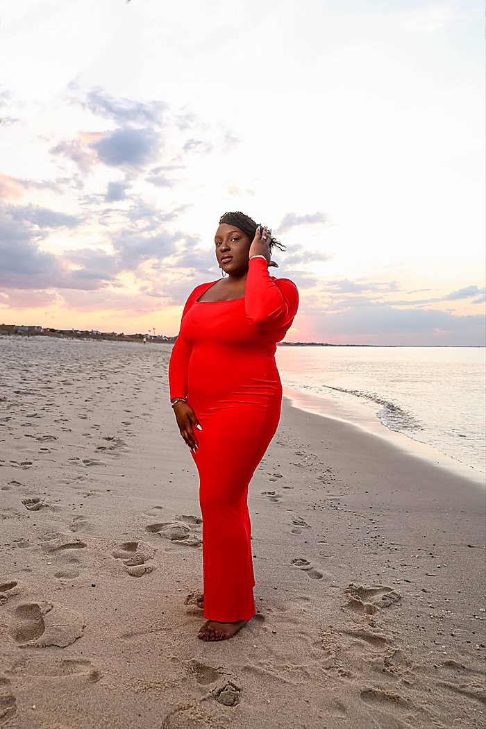 A full-length portrait on the beach at sunset: a red long-sleeved gown, footprints in the sand