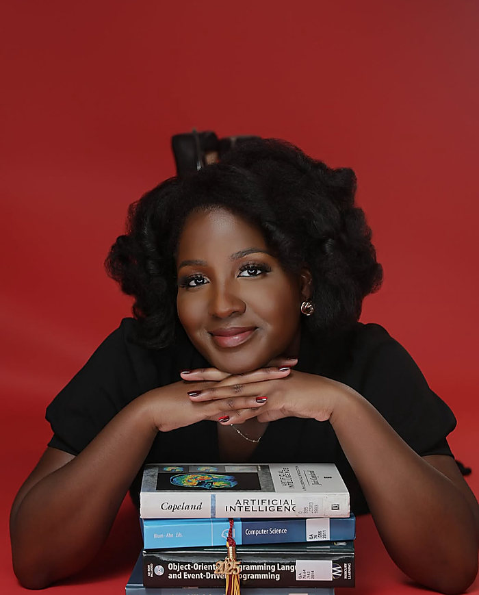 A portrait on a red backdrop: her chin on her hands over a stack of textbooks