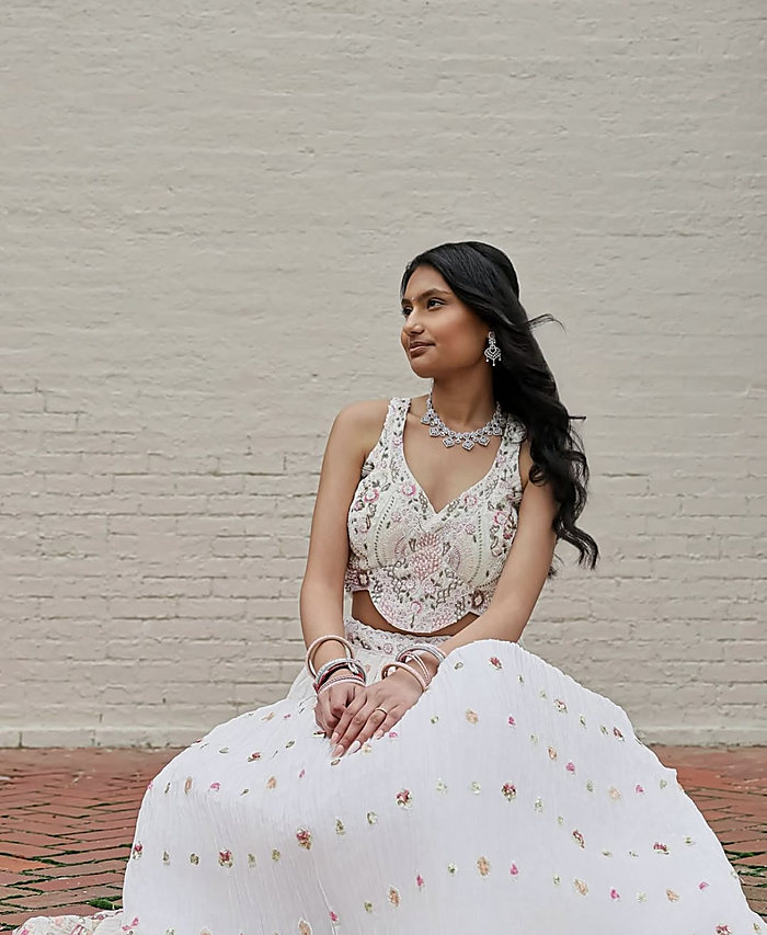 A seated portrait against a painted brick wall: a white embroidered gown