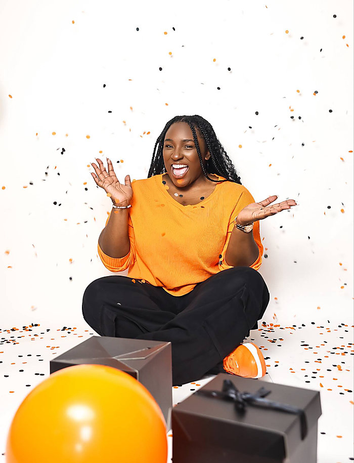 A birthday shoot on white: an orange sweater, confetti in the air, gift boxes and an orange balloon