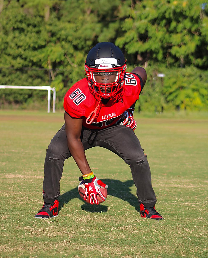 A football player in a red jersey and helmet, crouched in his stance on the field