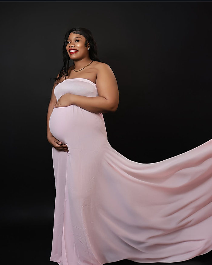 A maternity portrait on black: a blush pink gown with a long train held out
