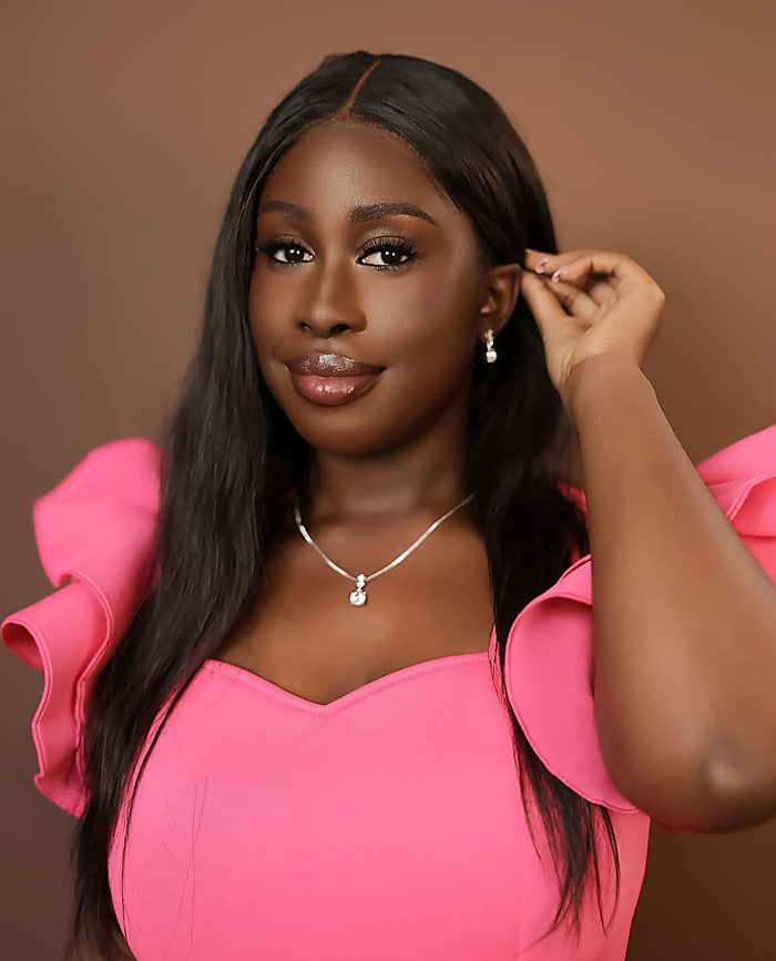A close portrait on a cocoa backdrop: a hot pink ruffled dress, one hand at her earring