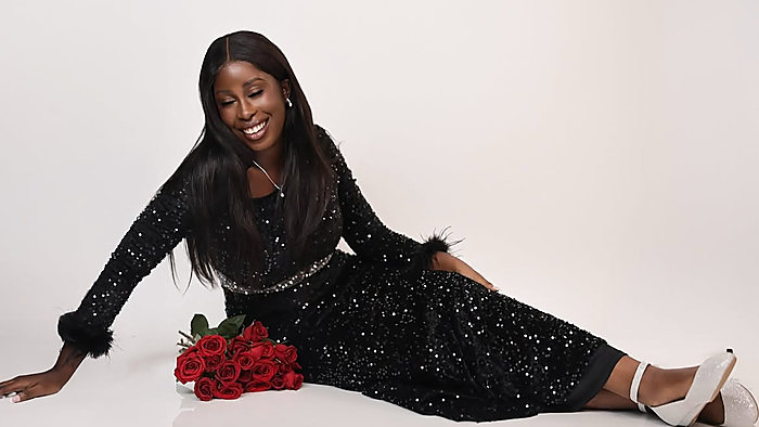 A birthday portrait on white: lying on the floor in a black sequin dress beside red roses